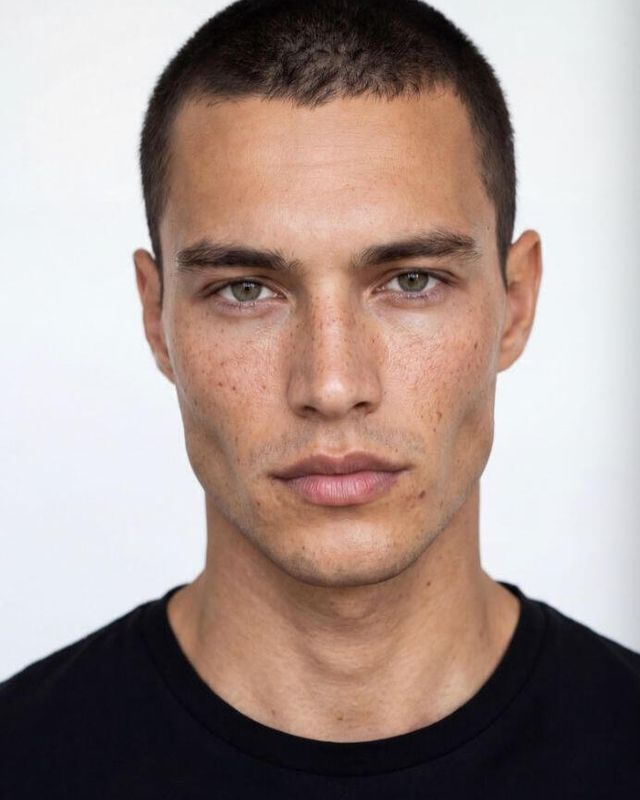 AI-generated portrait of a man with visible skin texture and freckles, front lighting against a plain background